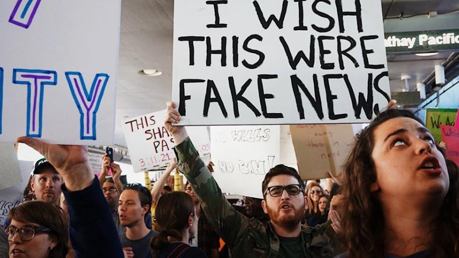 En flok mennesker, hvor en holder et skilt, hvor der står:"I wish this was fake news."