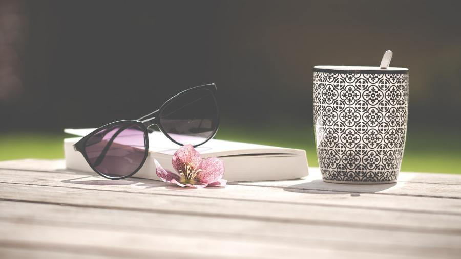 En bog med solbriller ovenpå og et kaffekrus ved siden af. 